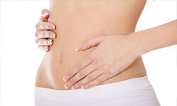 Picture of a girl with two hands touching her abdomen, showing her Abdominoplasty procedure.