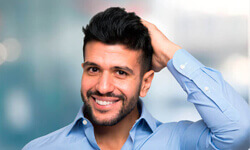 Portrait shot of a smiling man with his hand on his hair illustrating his hair replacement procedure.