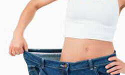 Front view photo of a woman standing in oversized jeans illustrating her weight loss with an obesity treatment.