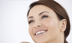 Angled photo of a smiling woman showing her happiness with a scalp reduction (forehead lift) procedure she had.