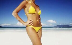 Picture of a slender woman standing on the beach with the ocean behind her, depicting her happiness with the pubic lift she had in Costa Rica.