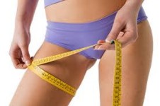 Front view photo of a woman holding a tape measure around her thighs illustrating the results of a thigh reduction procedure.
