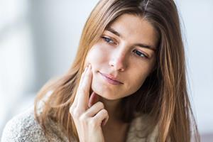 Picture of a woman holding a hand to the side of her chin, showing her happiness with the holistic temporo-mandibular treatment she had in Costa Rica.