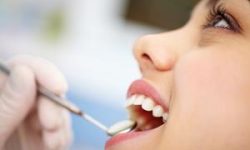 Picture of a smiling woman in a dental chair as a dentist is performing an oral surgery procedure.