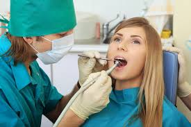 Picture of a smiling woman in a dental chair as a dentist is performing an oral surgery procedure.